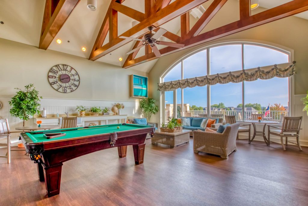 Spacious recreational room with wood beams, pool table, lounge seating, and large windows.