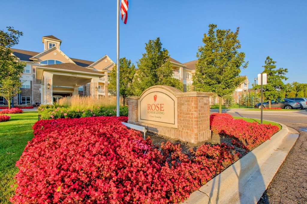 Front entrance of Rose Senior Living with bright flowers and an American flag
