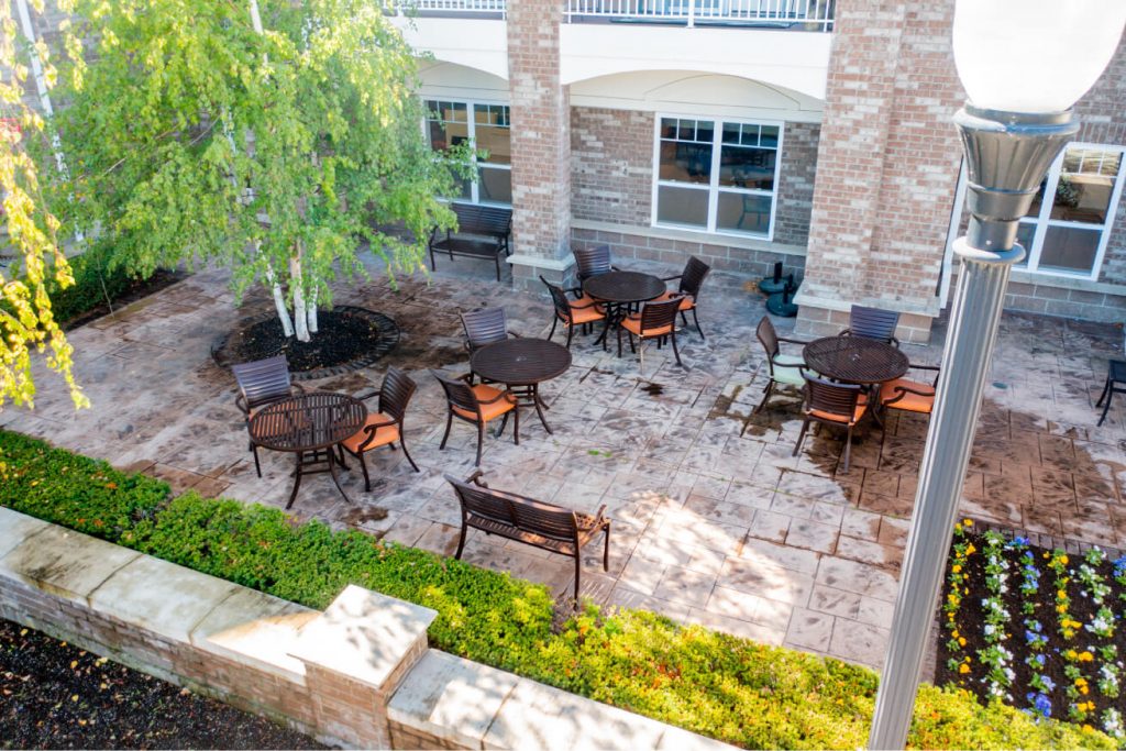 Aerial view of outdoor patio with tables, chairs, a bench, and lush greenery around.