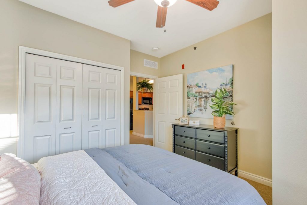 Bedroom with neutral walls, white doors, ceiling fan, and dresser with plant and painting
