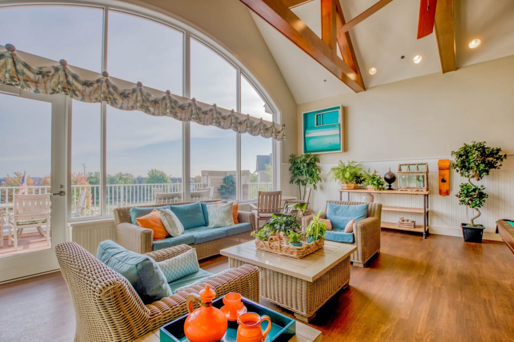 Bright sunroom with wicker furniture, large windows, vibrant cushions, and indoor plants.