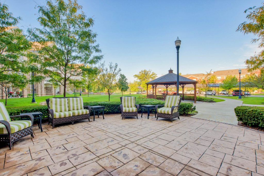 Outdoor patio with seating, trees, and a gazebo on a sunny day at a residential complex.