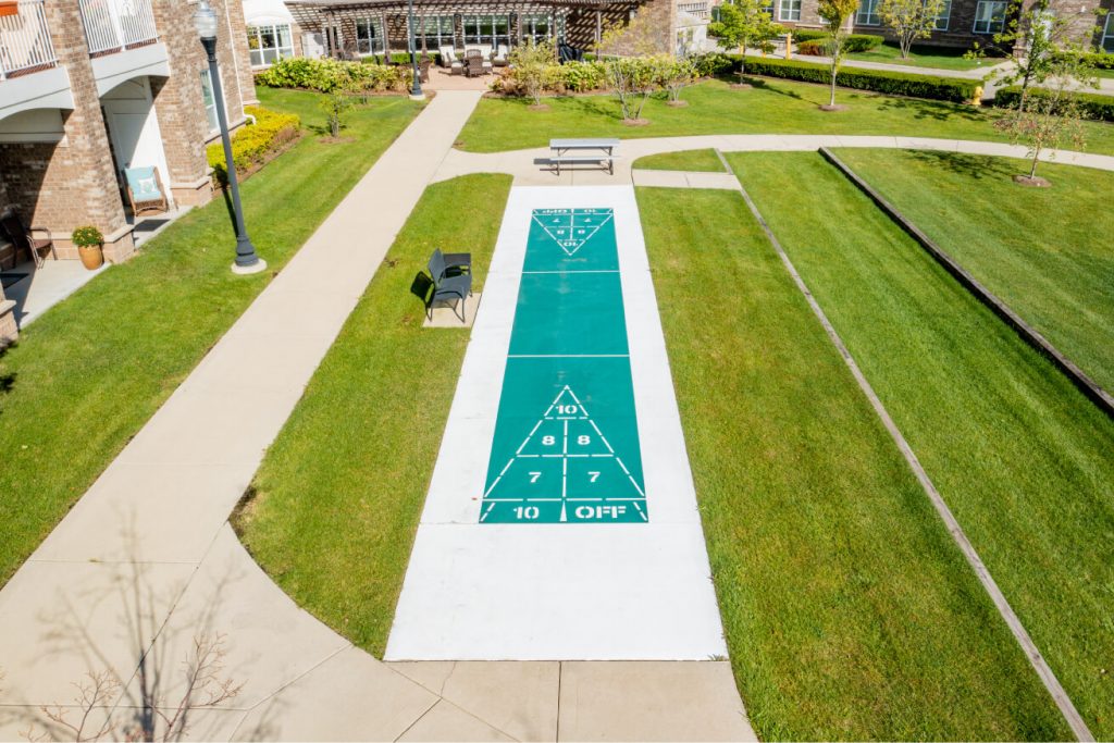 Outdoor shuffleboard court surrounded by green lawns and adjacent to residential buildings