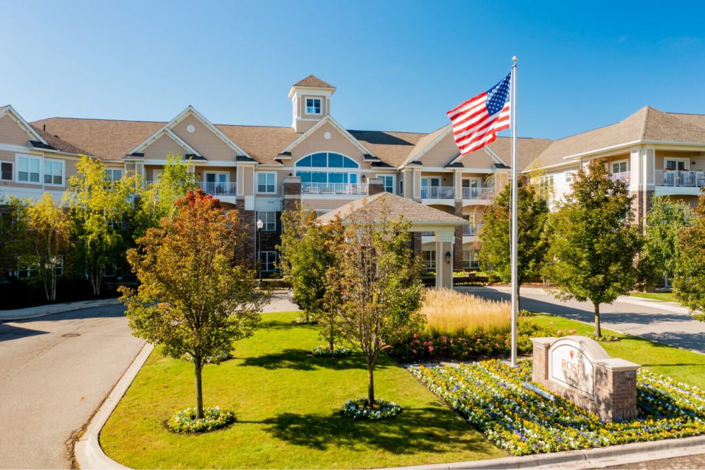 Three-story retirement residence with landscaped garden and an American flag waving in front yard.