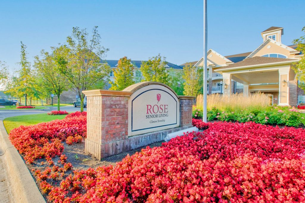 Rose Senior Living sign surrounded by red flowers at the entrance of a residential building