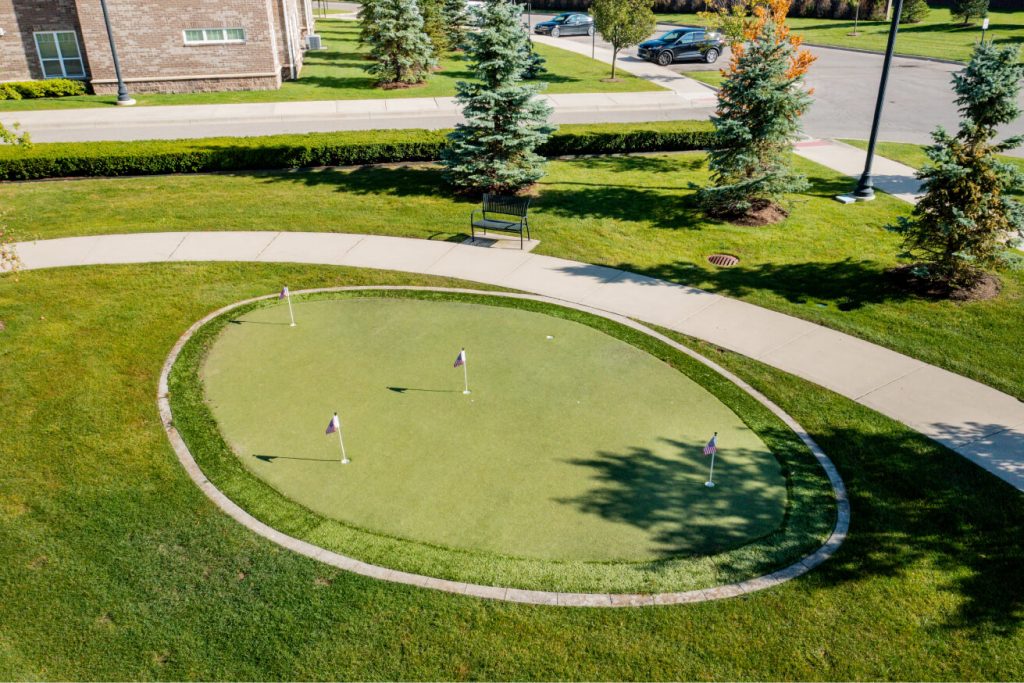 Aerial view of a small putting green with four flagsticks, surrounded by a paved walkway.