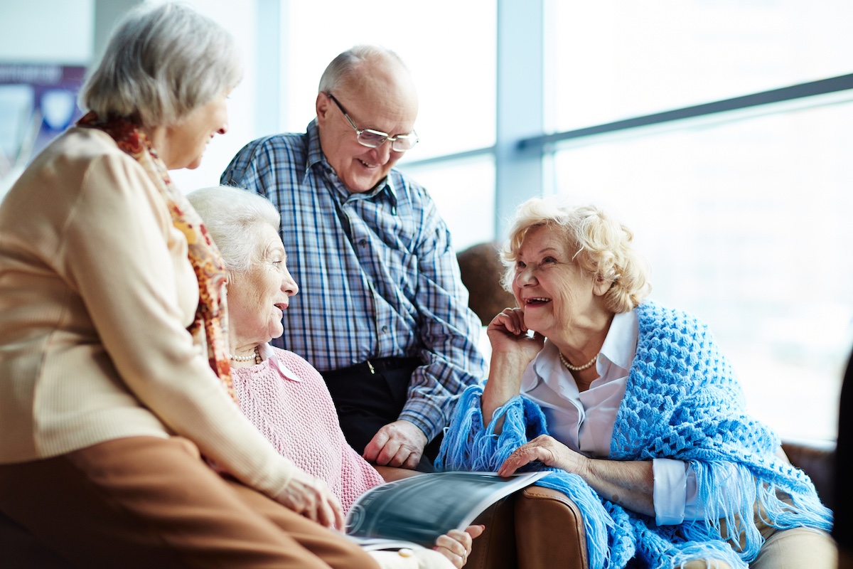 Group of elderly friends smiling and chatting while looking at a photo album indoors.