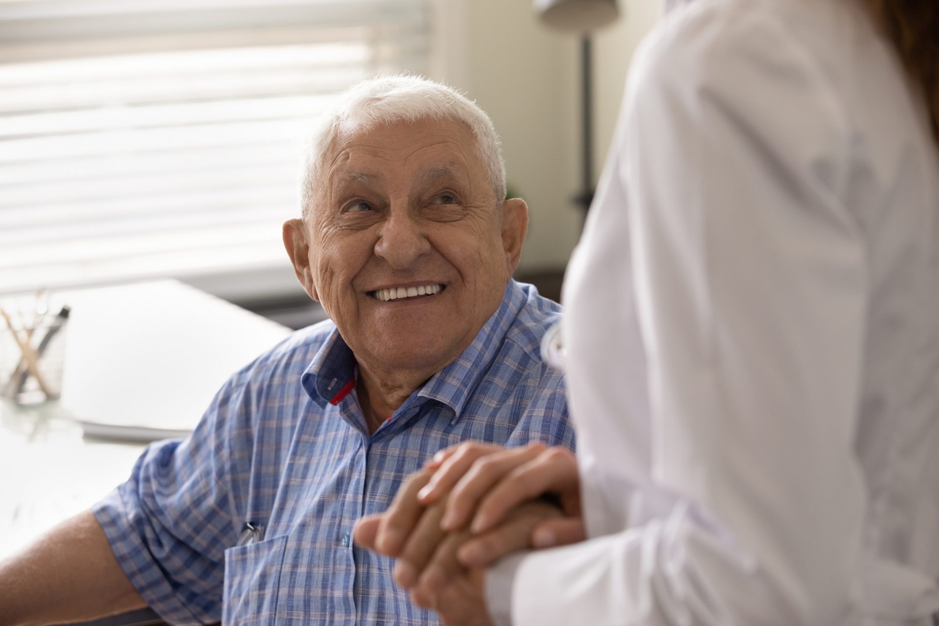 Elderly man smiling at a healthcare professional who is holding his hands